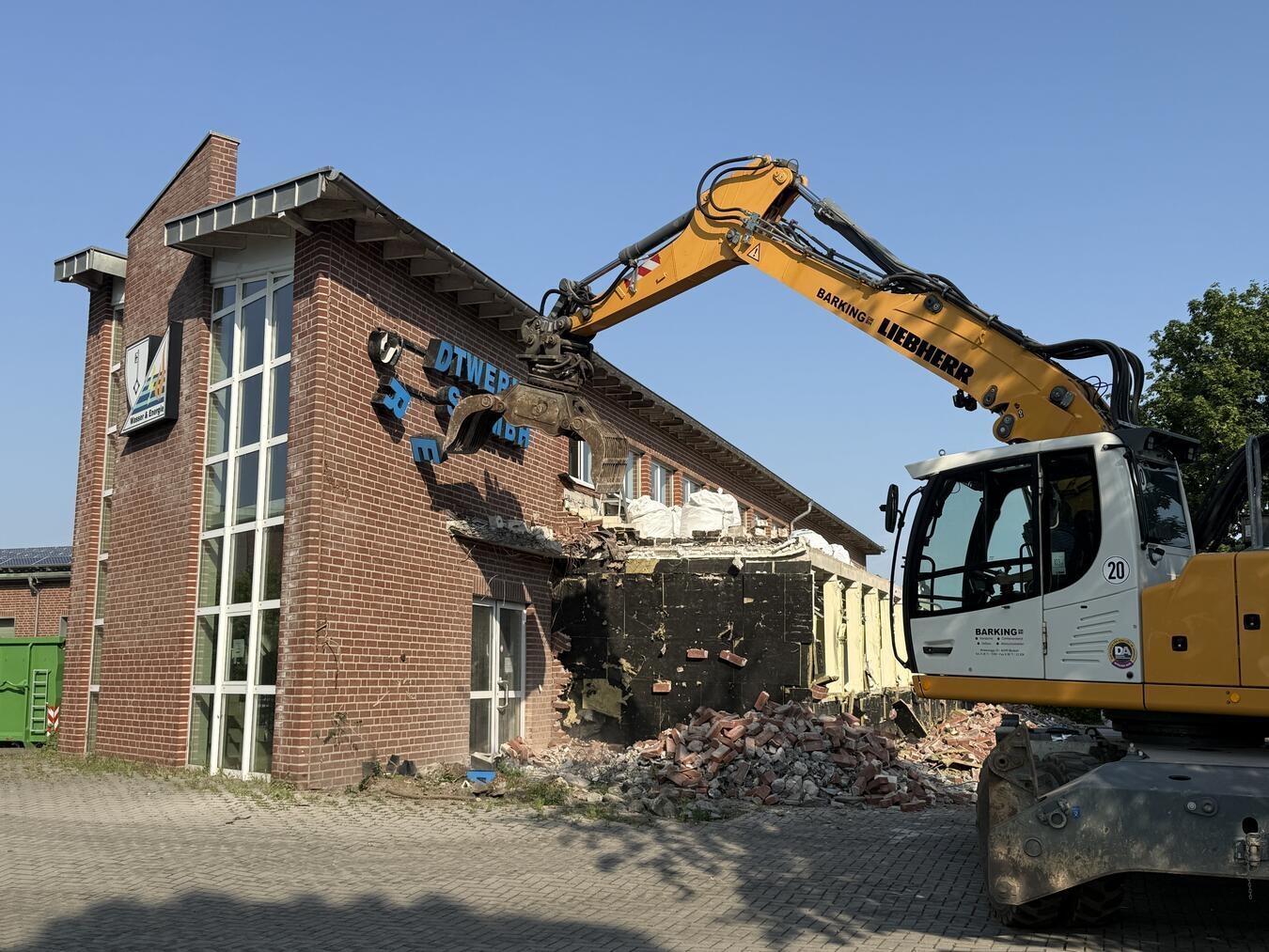 Abrissbagger reißt altes Verwaltungsgebäude der Reeser Stadtwerke mit Schriftzug und Firmenlogo ein.
