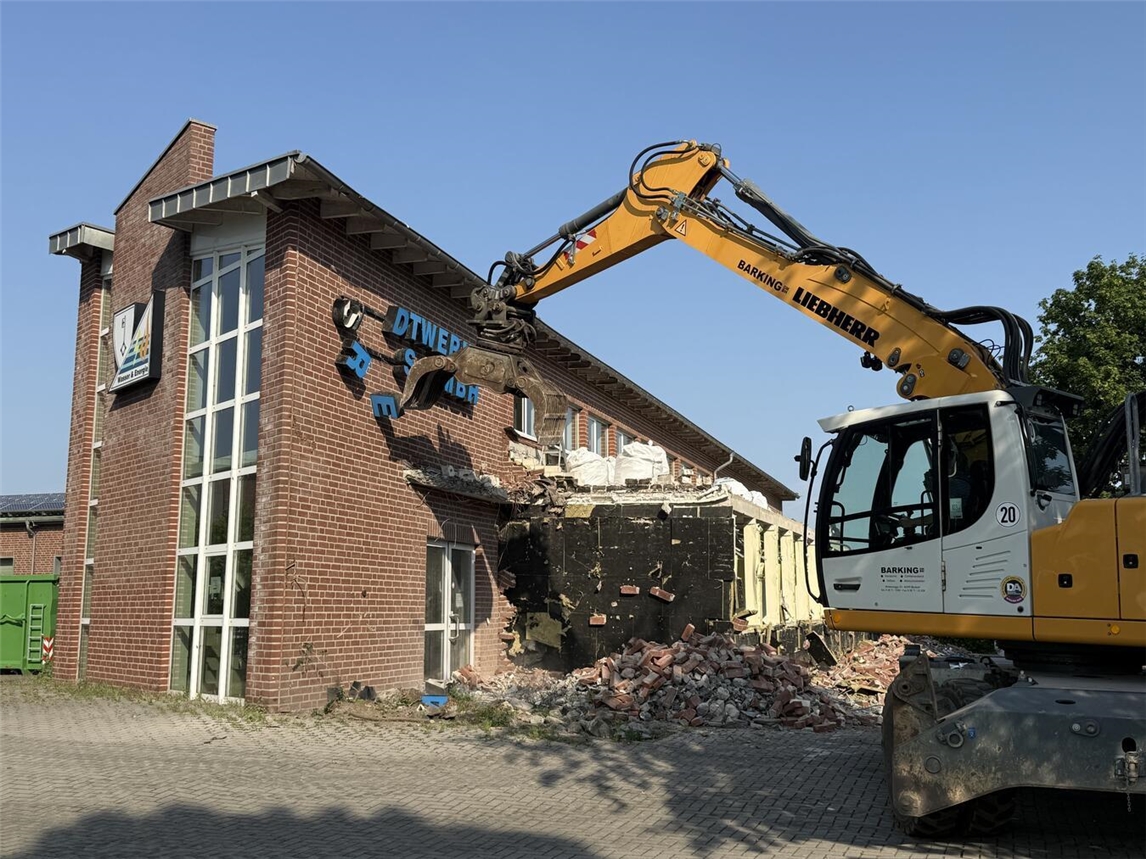 Abrissbagger reißt altes Verwaltungsgebäude der Reeser Stadtwerke mit Schriftzug und Firmenlogo ein.