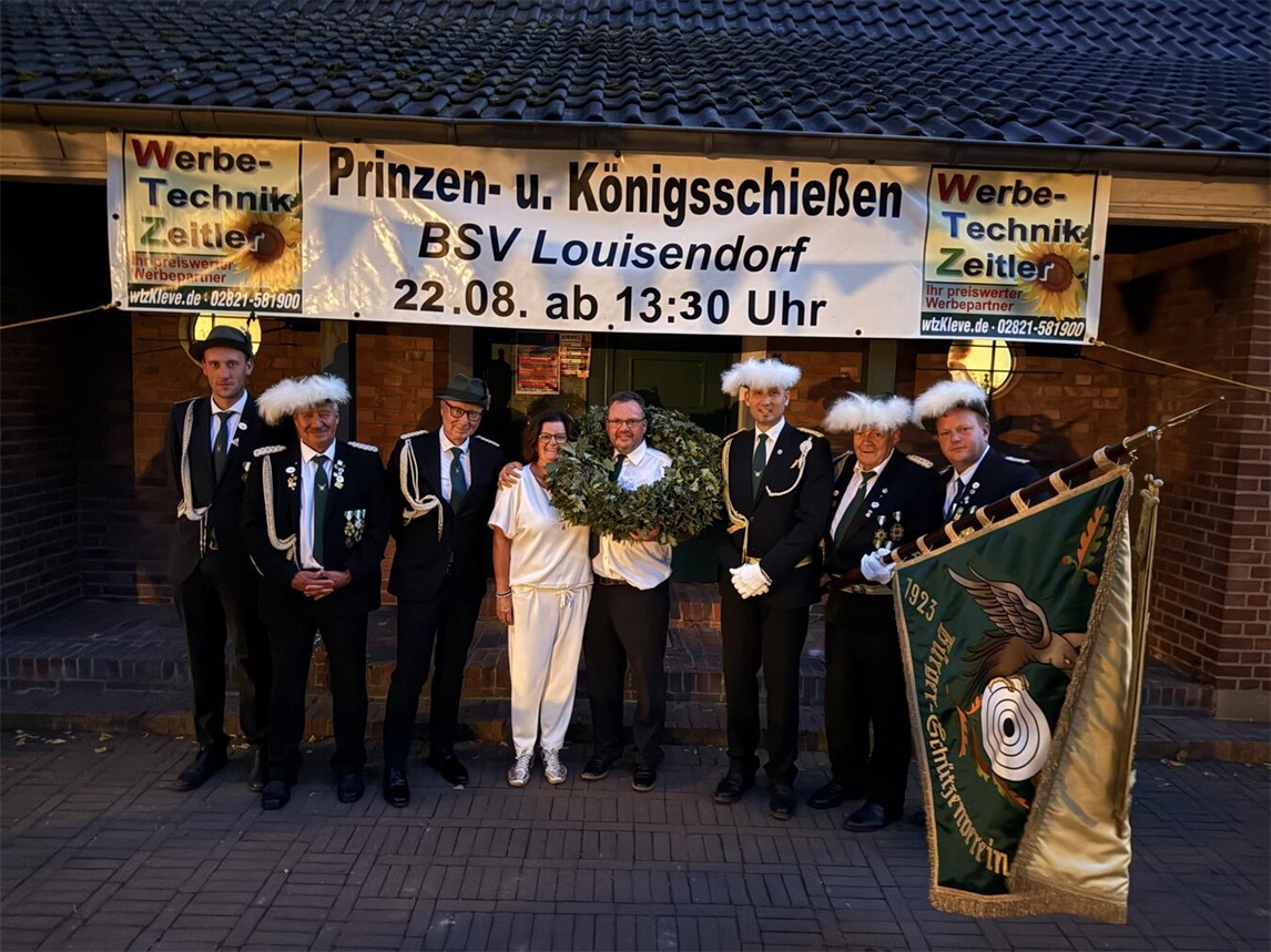 "Andreas und Melanie Mohn als Königspaar der Bürgerschützen Louisendorf, feierlich gekleidet, lächeln in die Kamera."