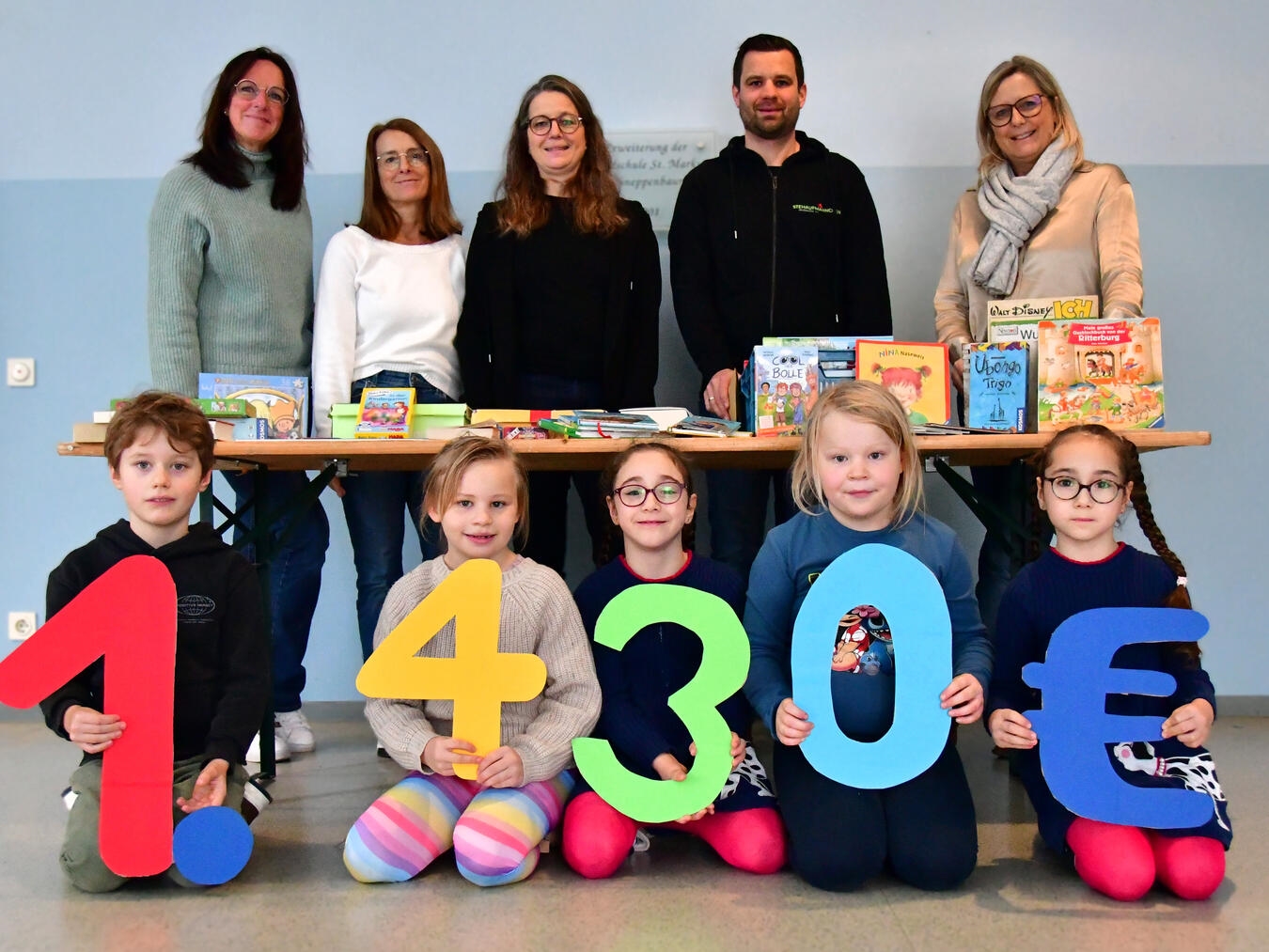 Anke Hüskes (v.l.n.r.), Bianka Lehnen, Veronika Schüßler und Manuela Witzke übergaben Peter Goemans vom Verein Stehaufmännchen die Spende. Die Kinder aus der OGS hielten die Spendensumme hoch. Foto: Caritas