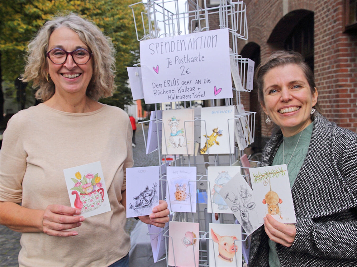 Annette Hagen, Leiterin der Stadtbücherei Kalkar (l.), und Stephanie Marzian (r.) mit den lustigen Postkarten, die nun für einen guten Zweck verkauft werden. NN-Foto: Theo Leie