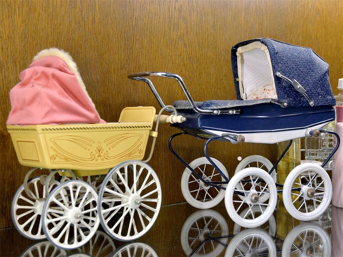 "Miniatur-Kinderwagen auf Holztisch, Detailaufnahme, Spielzeug, Deko, Puppenwagen"
