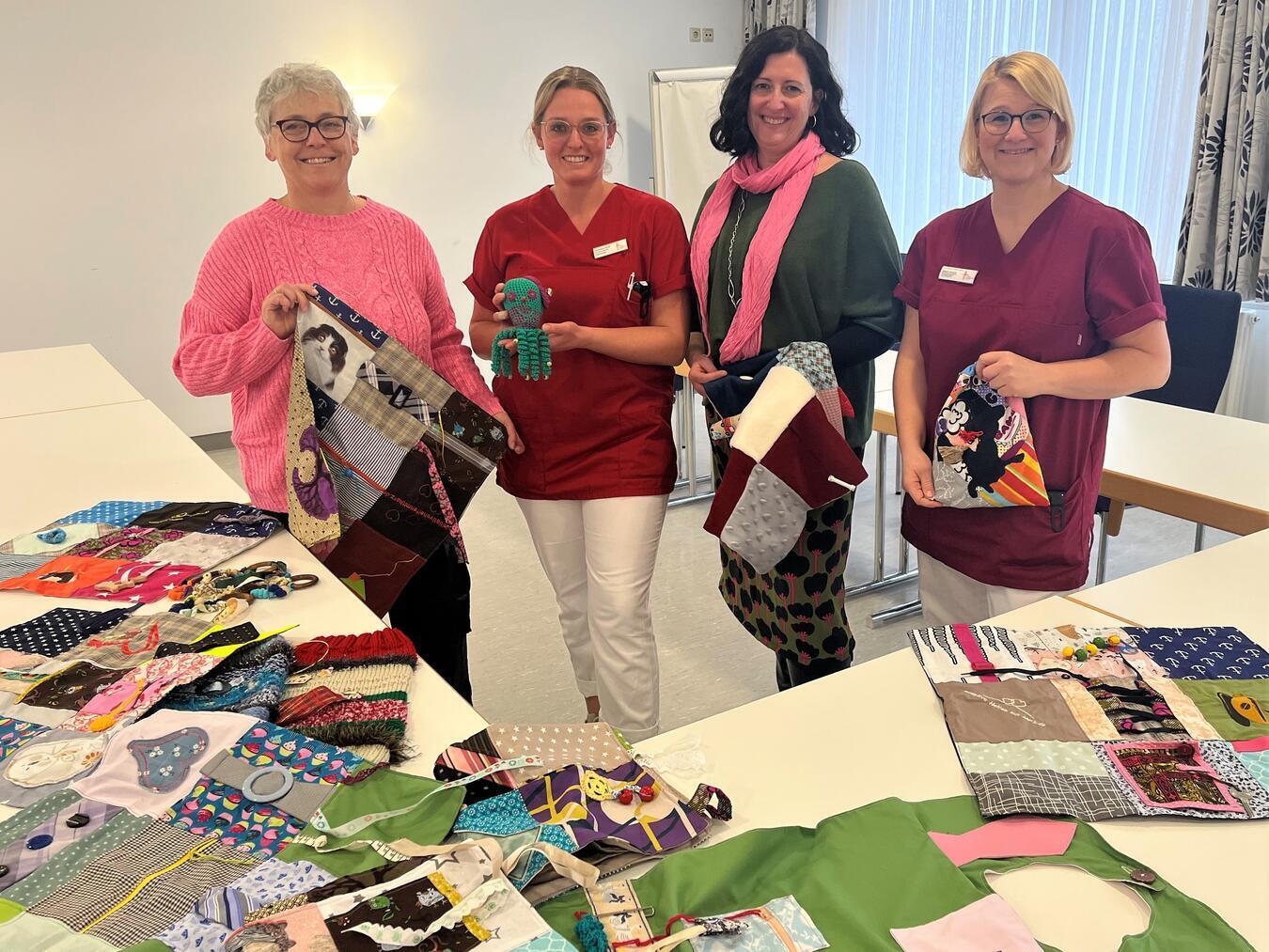Auch Pflegefachkraft Dagmar Brendel (r.) und Ergotherapeutin Christina Kroll in der Klinik für Altersmedizin und Frührehabilitation des St.-Clemens-Hospitals freuen sich über die Nesteldecken und -ringe für ihre Patientinnen und Patienten, die Sonja Martens (l.) und Jessica Döhrn von der Initiative Helfen mit Herz übergeben.