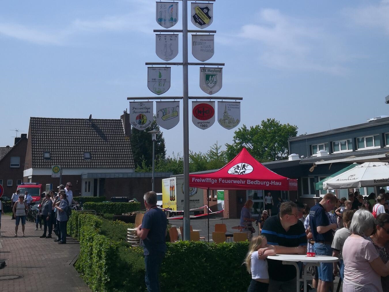 "Maifest auf Dorfplatz mit fröhlichen Menschen und bunten Ständen, Frühlingsfest im Freien"
