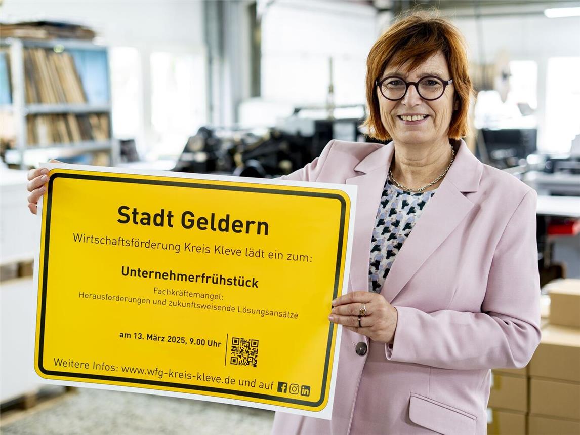 Brigitte Jansen, Geschäftsführerin der Wirtschaftsförderung Kreis Kleve, präsentiert das Ortsschild der Stadt Geldern mit der Einladung zum Unternehmerfrühstück.Foto: WfG Kreis Kleve