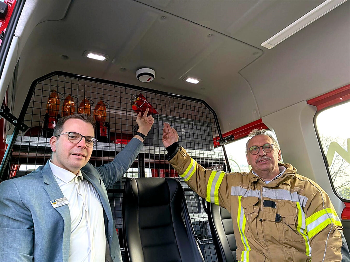 Bürgermeister Stephan Reinders (links) und Feuerwehrleiter Klaus Elsmann zeigen einen der neu installierten Rauchmelder im Mannschaftsraum eines Fahrzeugs. Die Technik soll Brände frühzeitig erkennen und die Sicherheit von Fahrzeugen und Gerätehäusern erhöhen. Foto: Feuerwehr Bedburg-Hau