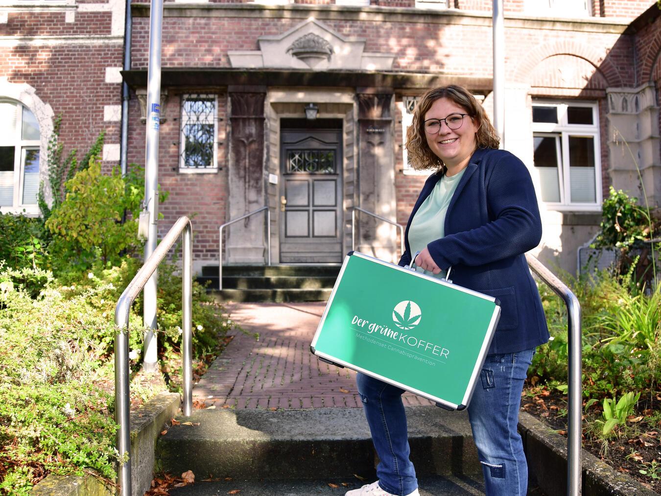 Caritas-Mitarbeiterin Jennifer Dellnitz von der Fachstelle für Suchtprävention mit dem „grünen“ Koffer vor dem Beratungszentrum an der Hoffmannallee in Kleve. Foto: privat