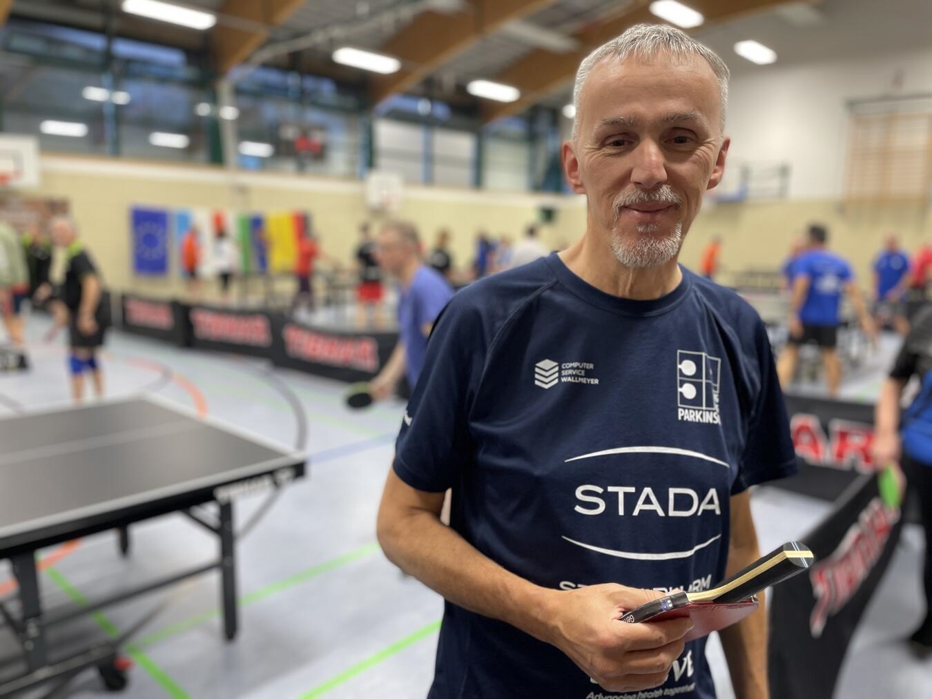 "Christopher Braun, Leiter PingPongParkinson-Stützpunkt Elten, lächelnd im Portraitfoto"