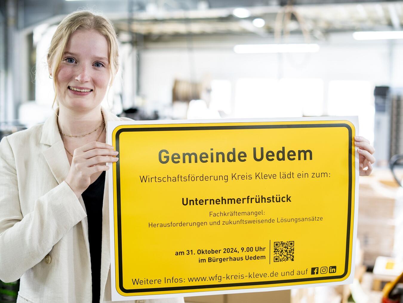 Corinna Strunk von der Wirtschaftsförderung Kreis Kleve präsentiert das Ortsschild der Gemeinde Uedem mit der Einladung zum Unternehmerfrühstück. Foto: Gerhard Seybert