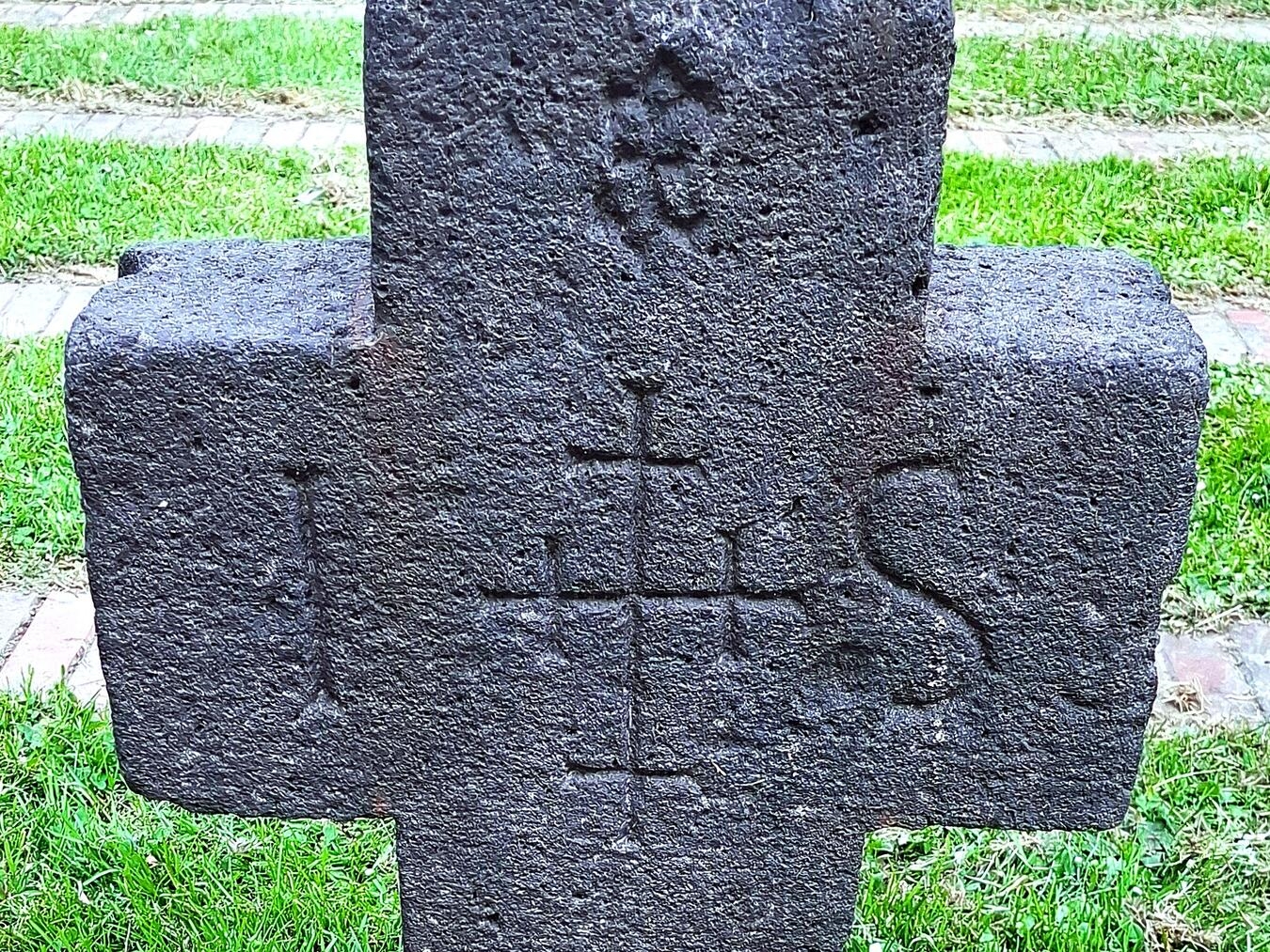 "Altes Basaltkreuz mit 'IHS', Kreuzen und Blüte, Grabsteininschrift verloren, historisches Denkmal."