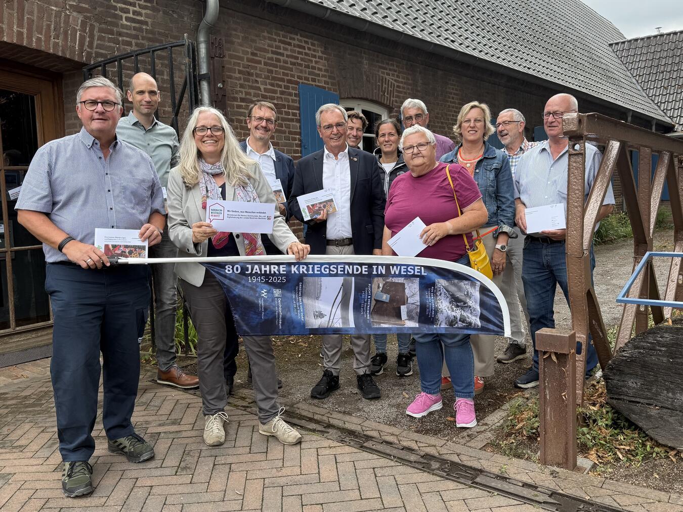 Das Gruppenfoto entstand vor einem Segment einer sogenannten „Bailey-Bridge“ – einer mobilen Notbrücke aus dem Zweiten Weltkrieg, die heute Teil der Dauerausstellung des Deichdorfmuseums ist. Foto: Liberation Route NRW