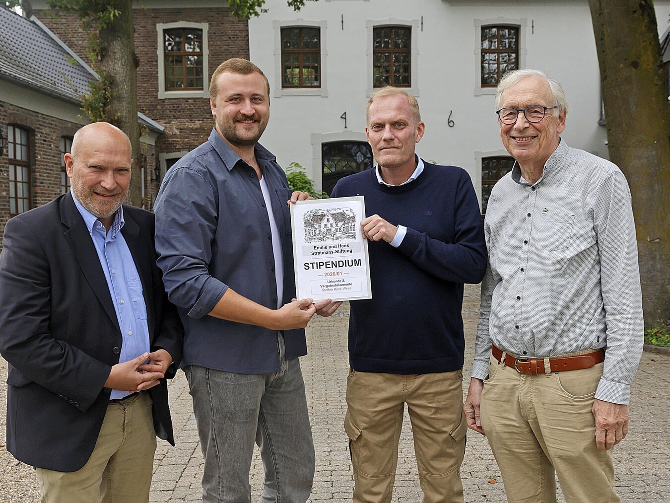 Vier Männer stehen nebeneinander bei einer Stipendienverleihung, darunter der erste Stipendiat und Vertreter des Historischen Vereins.