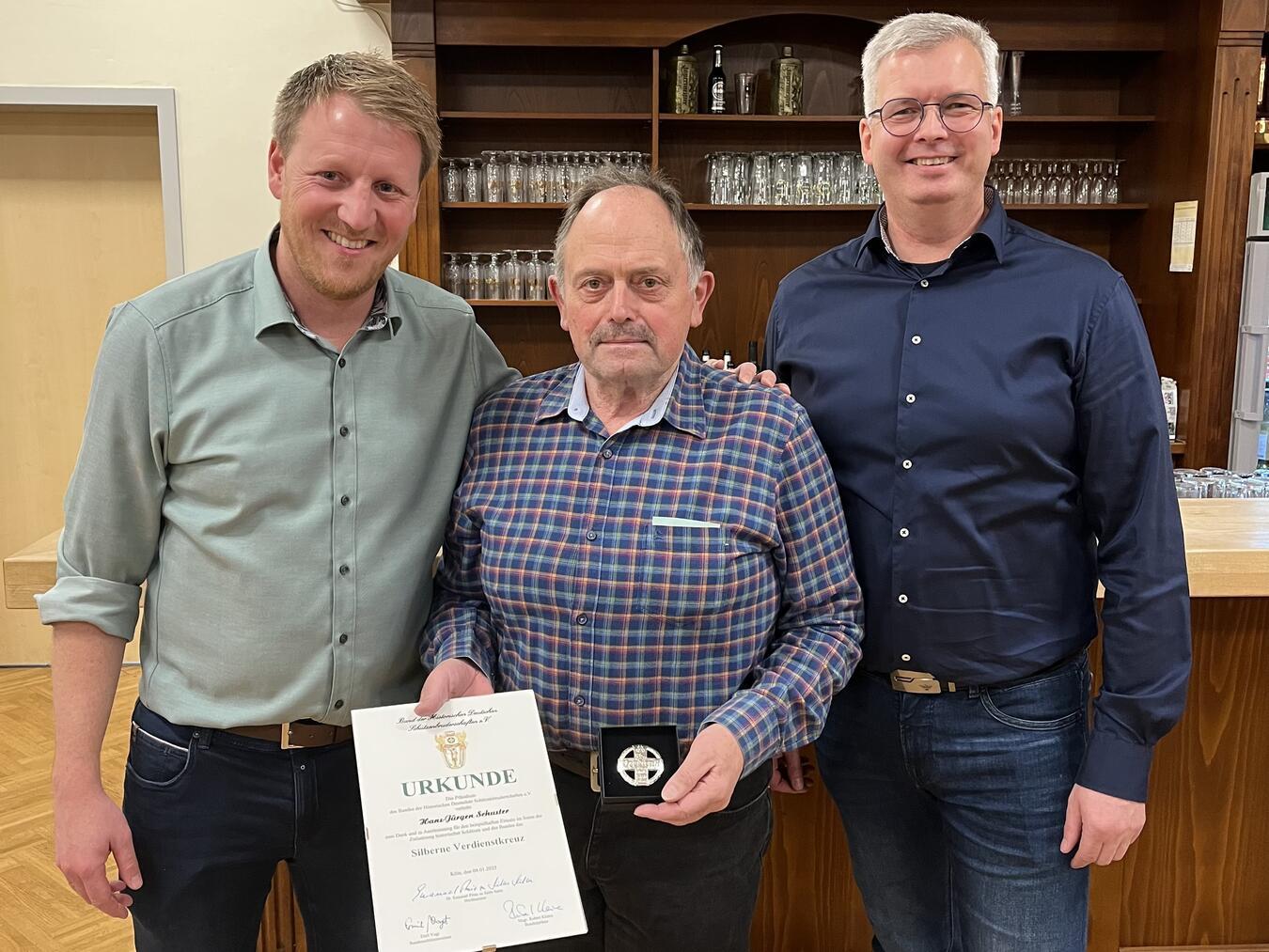 Der 1. Vorsitzende Klaus Theuvsen (r.) und der 2. Vorsitzende Christoph Cox (l.) ehrten Hans-Jürgen Schuster mit dem Silbernen Verdienstkreuz. 