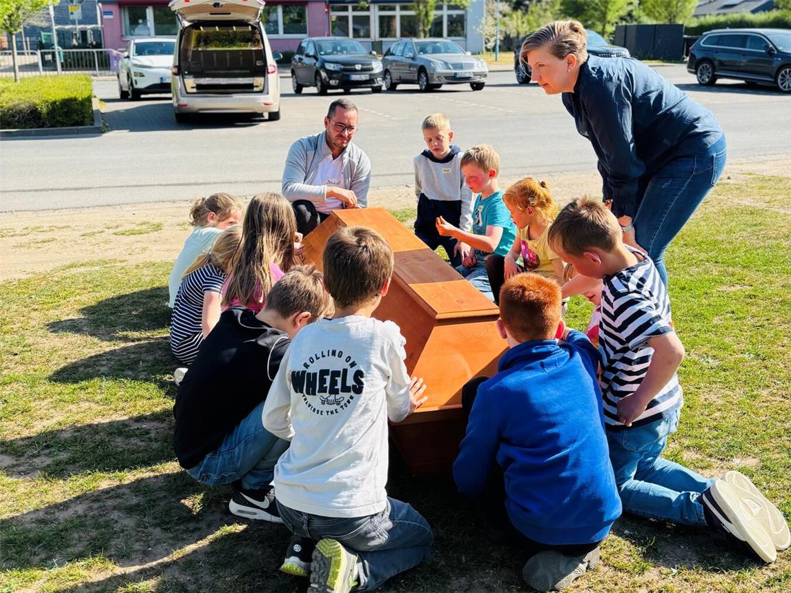 „Der Besuch des Bestatters war am coolsten“, sagte Ella (7). Ganz unbedarft und ohne Vorbehalte fassten die Kinder den hölzernen Sarg an und zogen ihn gemeinsam aus dem champagnerfarbenen Leichenwagen heraus. Foto: CV Kleve