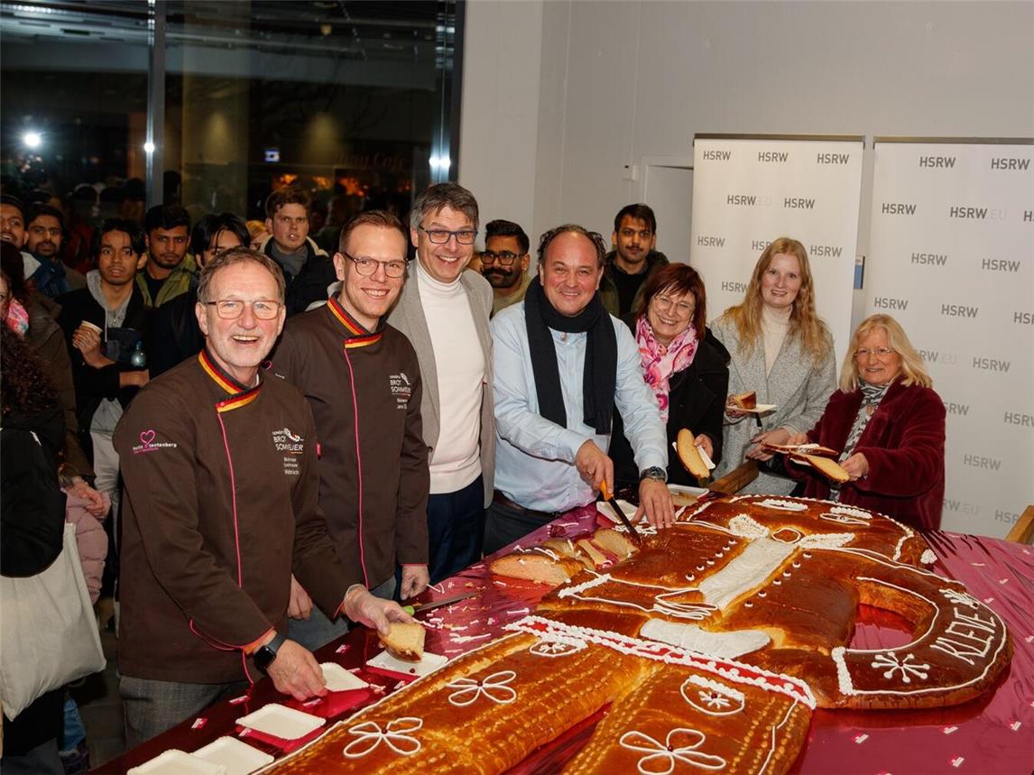 Der Präsident der Hochschule Professor Dr. Oliver Locker-Grütjen (3.v.l.) schneidet gemeinsam mit Robert Beinio (4.v.l.), Brigitte Jansen (5.v.l.), Monika Geenen (1.v.r.) und Corinna Strunk (2.v.r.) vom Förderverein Campus Cleve den von Walter und Christian Heicks (1. und 2.v.l.) gelieferten Riesen-Weckmann auf. Foto: Förderverein Campus Cleve/ Fotostudio Peschges