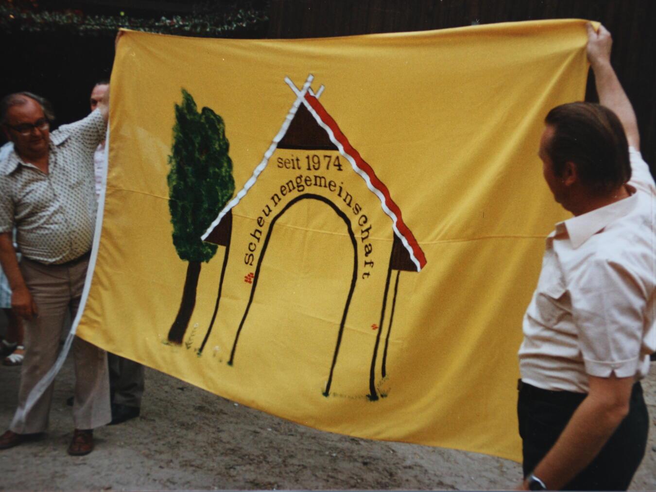 Die Fahne der Scheunenfest-Gemeinschaft wurde 1980 angefertigt und hängt bis heute, wenn die Nachbarn zusammen kommen. Hier im Bild: Hugo Herfurt (l.) und Gastgeber Josef Giesen (r.). Foto: privat