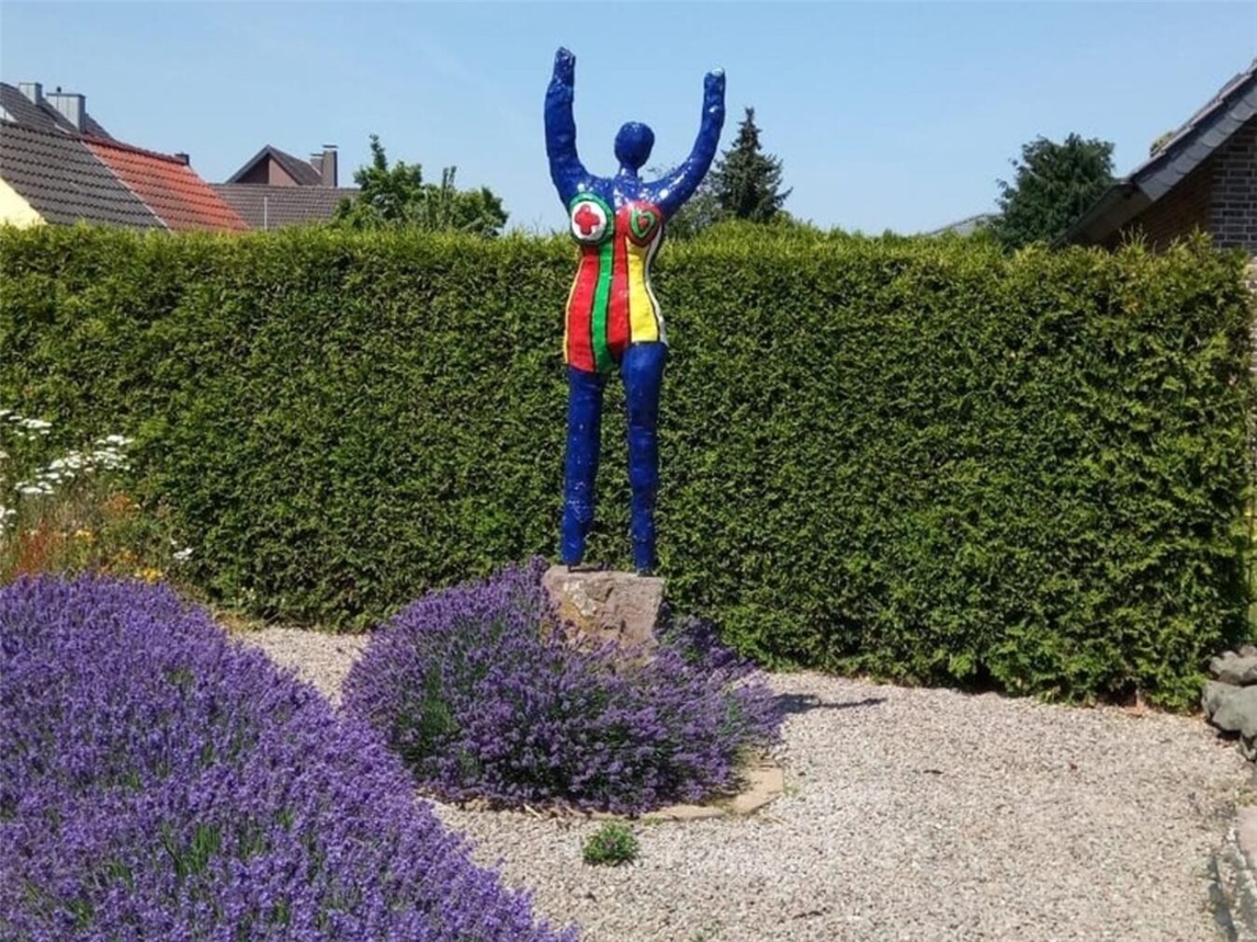 "Familie Pulheim und Gäste im Kunsthandwerks-Garten 'Emilies', einladende Atmosphäre, Besucher willkommen."
