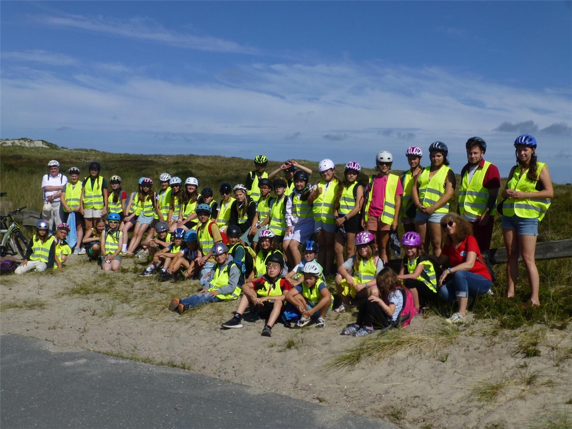 "Gruppe von Kindern und Betreuern mit Propst Notz auf Strandweg, fröhlicher Ausflug am Meer"