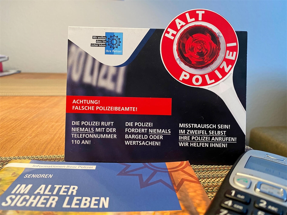 "Polizei warnt vor Telefonbetrug, Symbolbild mit Warnhinweis, Polizeiuniform im Hintergrund"