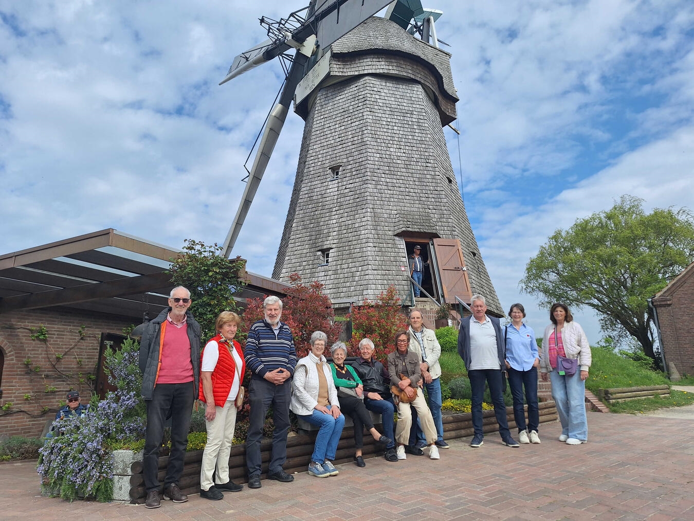 "Teilnehmer vor Mühle bei Sonnenschein mit Frühjahrsblumen, Frühlingsausflug"