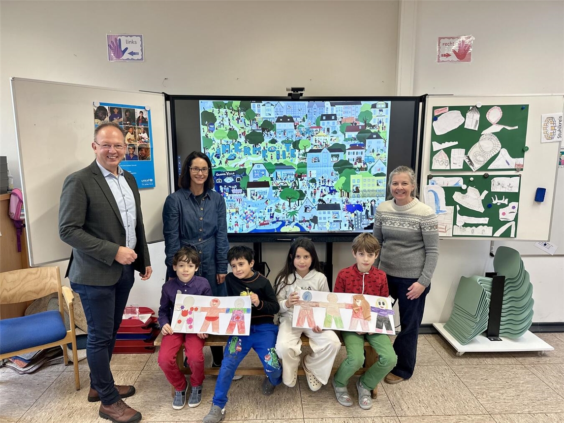 Die Veerter Grundschüler (v.l.n.r.) Tim und Kian (2. Klasse), Amilia (4. Klasse) und Jan (3. Klasse) präsentieren Markus Grönheim (Beigeordneter der Stadt Geldern), Schulleiterin Daniela Claßen (hinten links) und der stellvertretenden Schulleiterin Simone Meerkamp (r., projektverantwortlich mit Lehrerin Sabine Oerding) ihre in der Projektwoche gestaltete „Kinderkette“.Foto: Stadt Geldern/Terhorst