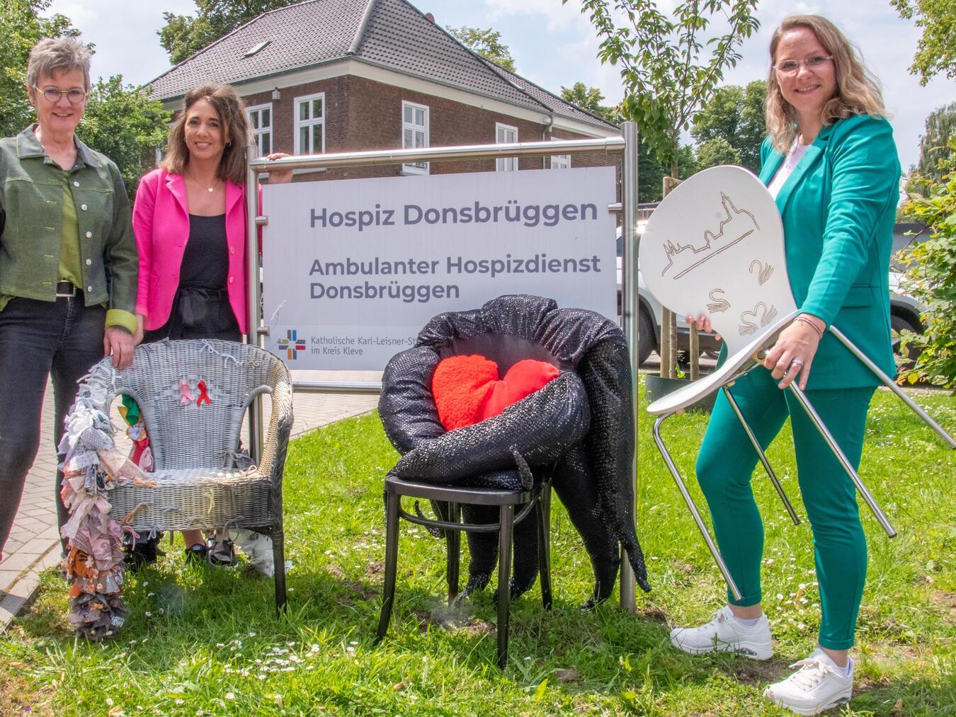 Dorothee Beutler, Jennifer Welles und Marion Aryus (v.l.) mit einigen der kunstvoll gestalteten Stühle, die beim Fest an der Wasserburg Rindern versteigert werden. Foto: Bischöfliche Pressestelle / Christian Breuer