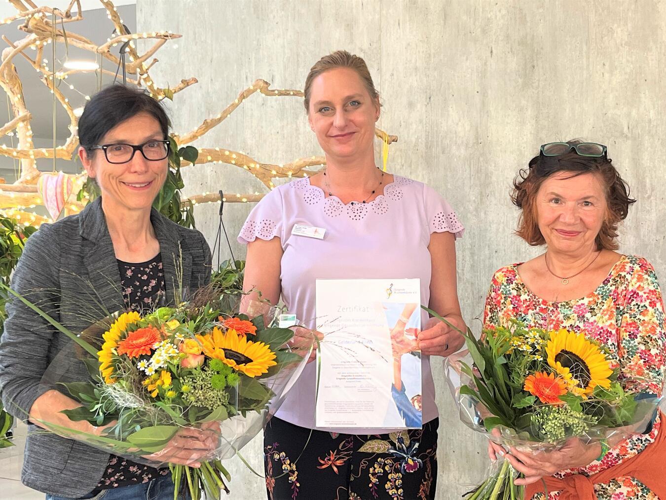 Dr. Pahl-Wurster (v. li.), Oberärztin und zertifizierte Singleiterin, und Dr. med. Sonja Höhndorf, Ärztliche Direktorin und Chefärztin der Gelderland-Klinik, nehmen das Zertifikat der Gelderland-Klinik als „Singende Gesundheitseinrichtung“ von Carmen Schroeder-Meißner, Vertreterin des Vereins Singende Krankenhäuser, entgegen.Foto: Gelderland-Klinik Geldern