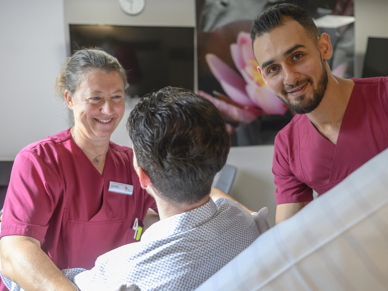 Eine Pflegekraft und eine Auszubildende als Pflegefachkraft begleiten eine Frau im Rollstuhl auf eine Station im St.-Clemens-Hospital.Foto: St.-Clemens-Hospital Geldern