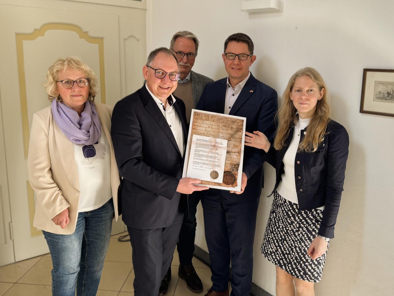 Eine Urkunde aus dem 12. Jahrhundert über „Smithusen“ für „Haus Schmithausen“, Sitz der Euregio Rhein-Waal, mit beigefügter Erklärungstafel gab es als Geschenk von der Stadt Rees: (v. li.) Tina Oostendorp (Stadtarchiv Rees), Sebastian Hense (Bürgermeister Rees), Veit Veltzke (Hansebeauftragter Rees), Andreas Kochs (Geschäftsführer Euregio Rhein-Waal) und Heidi de Ruiter (stellvertretende Geschäftsführerin). Foto: Stadt Rees