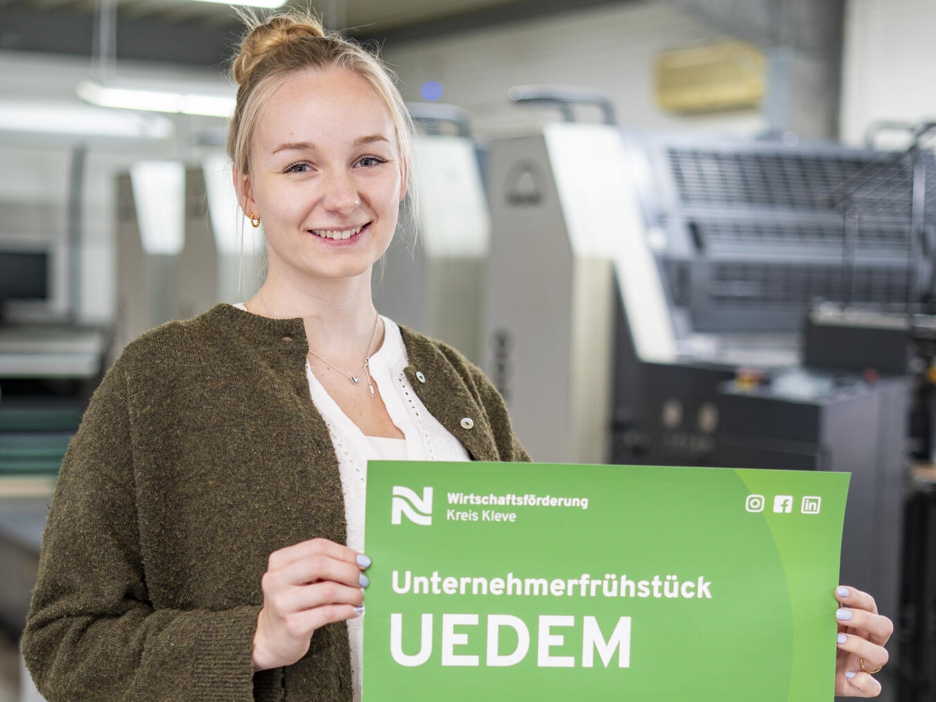 Emma Korn von der Wirtschaftsförderung Kreis Kleve präsentiert das Plakat mit der Einladung zum Unternehmerfrühstück in Uedem. Foto: Kreis-WfG/Gerhard Seybert