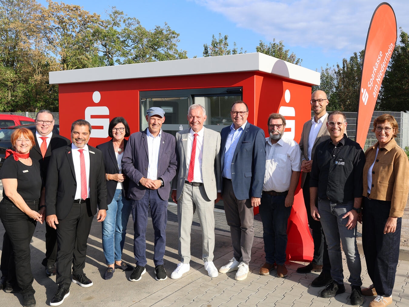 Eröffneten den neuen Sparkassen-Kubus auf dem Parkplatz von Edeka Luft in Alpen-Menzelen (v.l.n.r.): Carmen Müller, Lars Kisters und Giovanni Malaponti von der Sparkasse, die stellvertretende Bürgermeisterin Petra Bockstegers, Ortsvorsteher Sascha Angenendt, Bernd Zibell (Sparkasse), Frank Berger, der Verwaltungs- und Beiratsvorsitzende der Sparkasse, Beiratsmitglied Peter Nienhaus, Bürgermeister Ludger Staymann sowie Thomas und Ute Luft. Foto: Sparkasse am Niederrhein