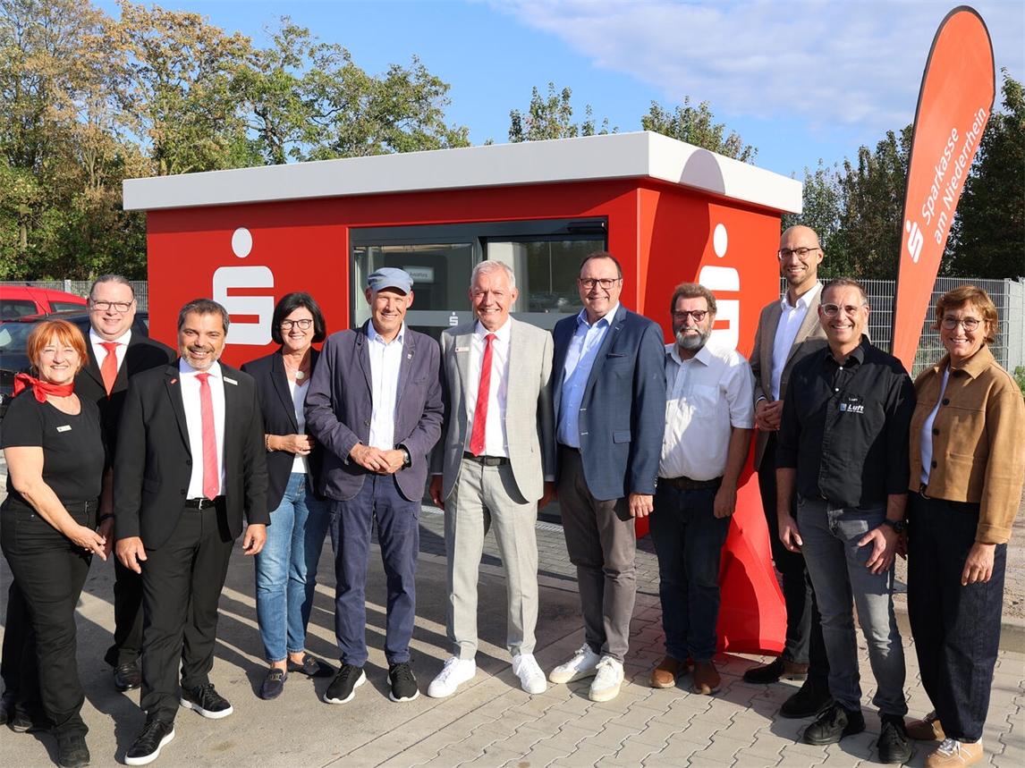 Eröffneten den neuen Sparkassen-Kubus auf dem Parkplatz von Edeka Luft in Alpen-Menzelen (v.l.n.r.): Carmen Müller, Lars Kisters und Giovanni Malaponti von der Sparkasse, die stellvertretende Bürgermeisterin Petra Bockstegers, Ortsvorsteher Sascha Angenendt, Bernd Zibell (Sparkasse), Frank Berger, der Verwaltungs- und Beiratsvorsitzende der Sparkasse, Beiratsmitglied Peter Nienhaus, Bürgermeister Ludger Staymann sowie Thomas und Ute Luft. Foto: Sparkasse am Niederrhein