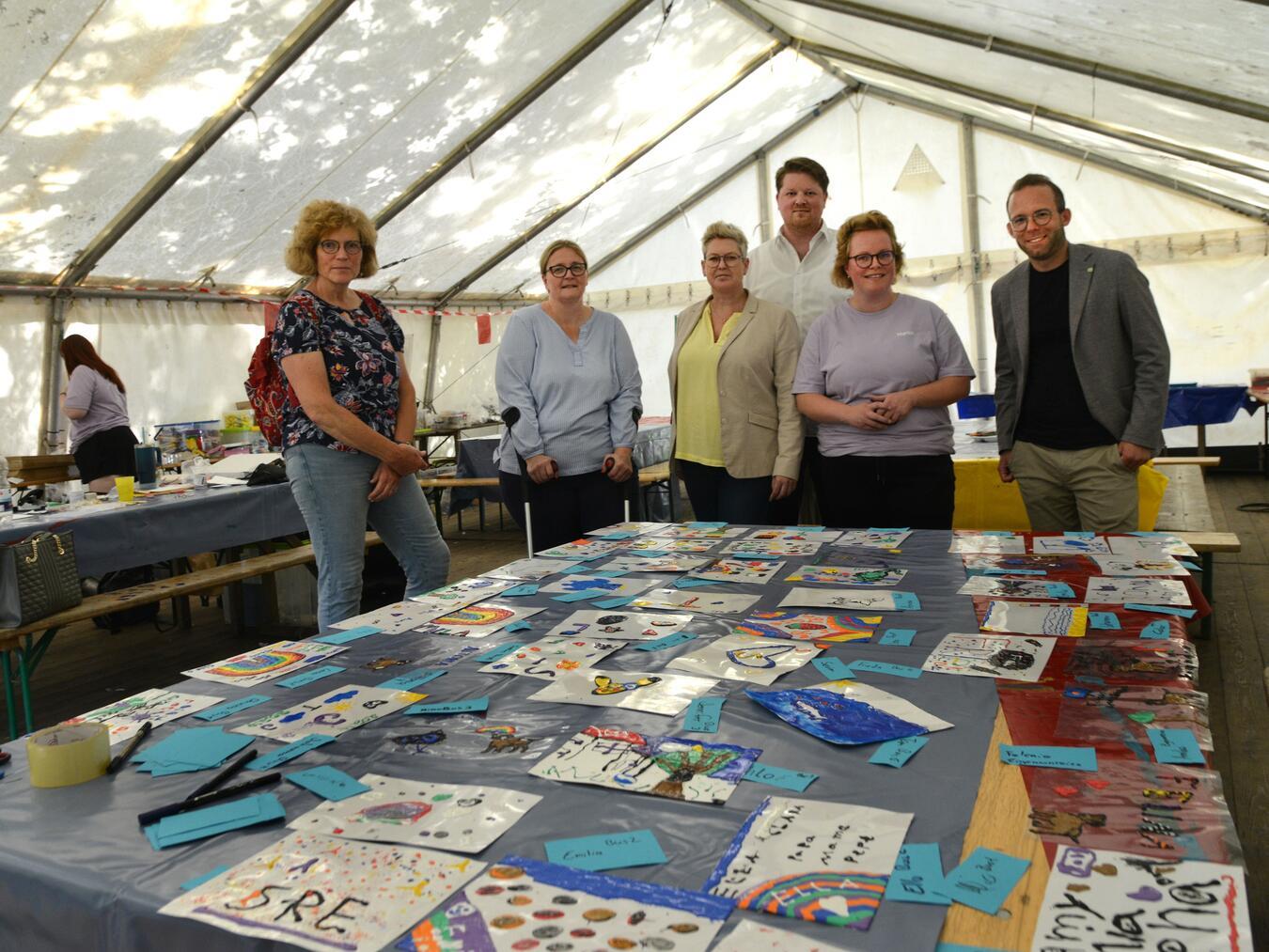 Erste Ergebnisse des Kreativ-Workshops zeigte Marion Janßen (2.v.r.), Leiterin von „Huck-ale-le“, den Besuchern bei der Stadtranderholung am Eyller See: David Kerkenhoff-Szopinski (3.v.r.), zweiter stellvertretender Landrat, Andrea Schwan (3.v.l.), Fachbereichsleiterin Jugend, Soziales und Jobcenter, sowie Andre Amourette (r.), Leiter der Abteilung Jugend und Familie, und Petra Gerits (l.), Vorsitzende des Jugendhilfeausschusses und Patricia Gerlings-Hellmanns (2.v.l.), beratendes Ausschuss-Mitglied.Foto: Kreis Kleve / Klaus-Dieter Stade
