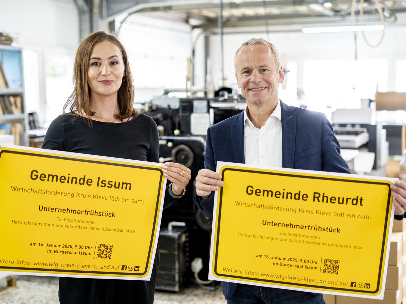 Fee Knupp und Dr. Benedikt Rösen von der Wirtschaftsförderung Kreis Kleve präsentieren die Ortsschilder der Gemeinden Issum und Rheurdt mit der Einladung zum Unternehmerfrühstück.Foto: WfG Kreis Kleve