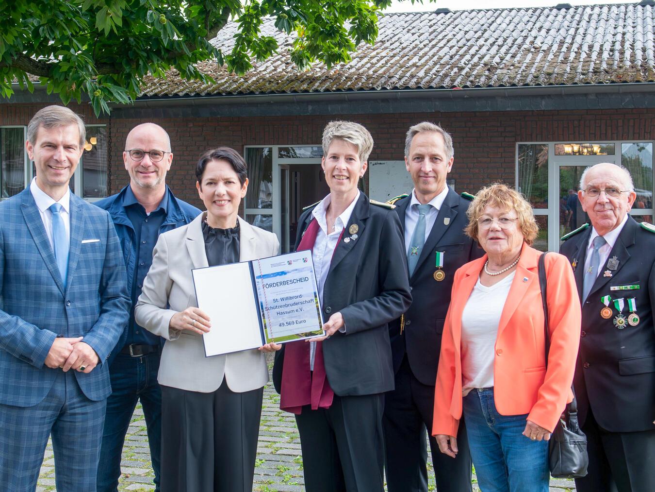 Landwirtschaftsministerin Silke Gorißen überreicht Förderbescheid für Dachsanierung des Dorfgemeinsc Förderbescheid für die St. Willibrord-Schützenbruderschaft Hassum (v. l.): Stephan Wolters (MdL), Stepah Luyven (Ratsmitglied), Ministerin Silke Gorißen, Isabel Luyven (Brudermeisterin), Ingo Wischinski (Schützenbruderschaft), Anna Peters (1. stellvertretende Bürgermeisterin) und Leo Schoonhoven (Schützenbruderschaft). NN-Foto: Gerhard Seybert