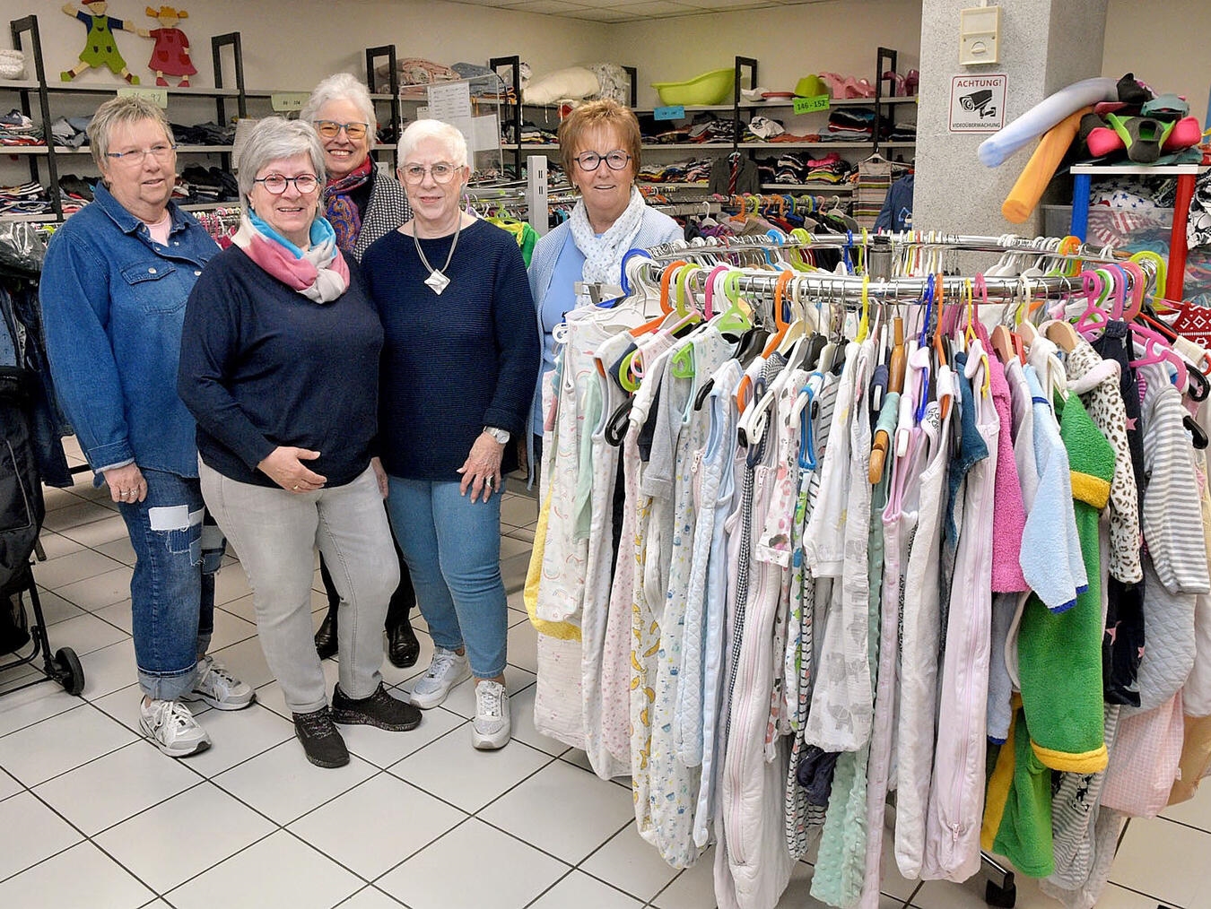 Gruppenfoto ehrenamtlicher Helferinnen im Ladenlokal der Kinderkiste, lächelnd vor Regalen, Fototermin mit Susanne Eis und Team.