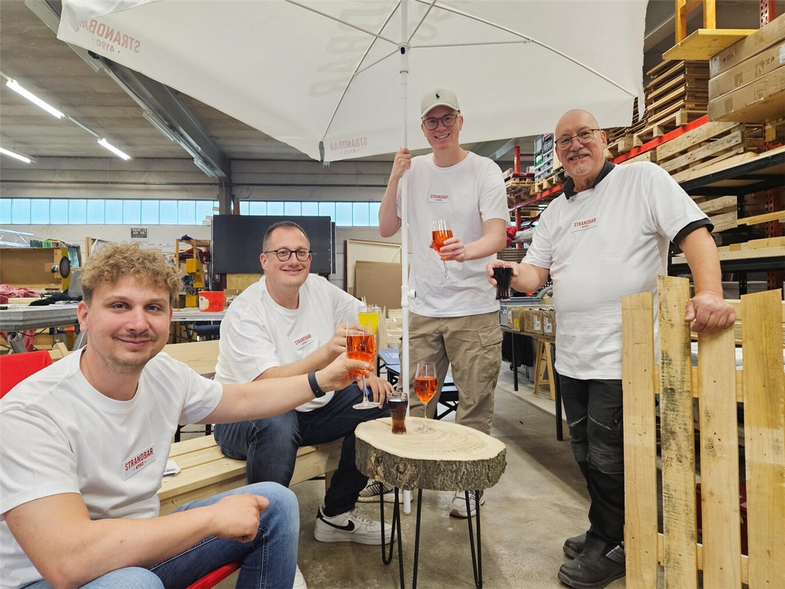 "David Göcking und Tobias Budde planen Social Media für Strandbar, während Tim und Dieter Tripp Möbel bauen."