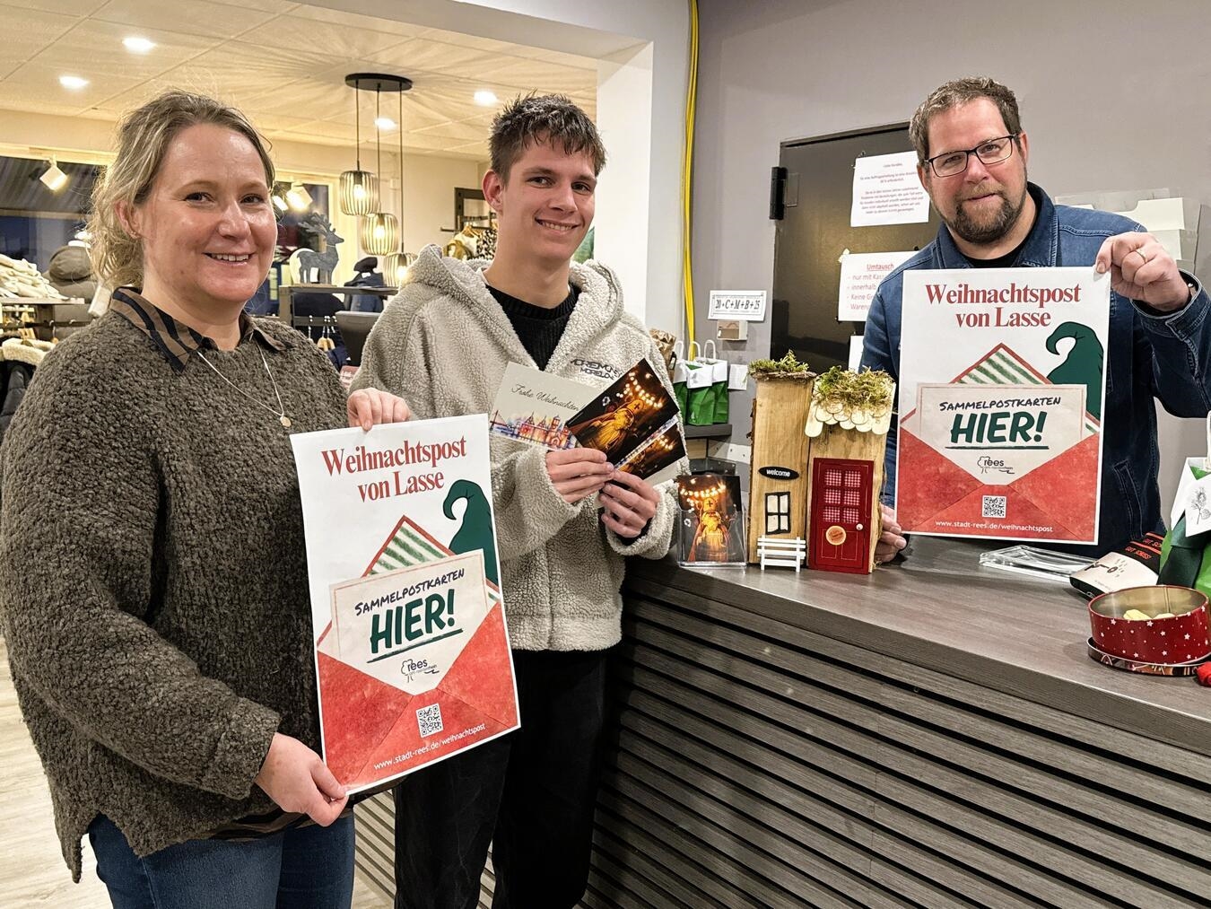 Für die Weihnachts-Sammelpostkarten werben (v. li.) Annette Kook (Stadtmarketing), Matthias Dahmen (Auszubildender Stadt Rees) und Michael Rose (Bekleidungshaus Wessendorf). Foto: Stadt Rees