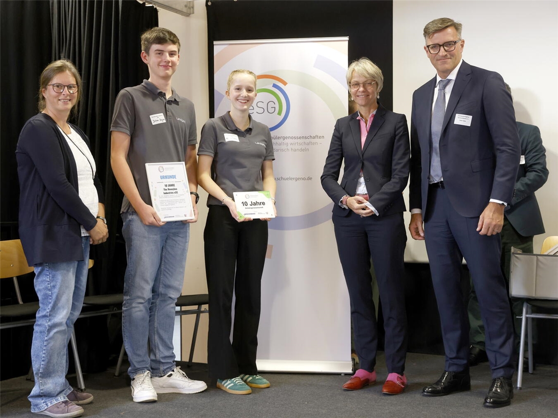 Große Freude bei der Schülergenossenschaft „The Honeybee Industries eSG“: Sie wurdevon NRW-Schulministerin Dorothee Feller (2.v.r.) und Peter Götz, Vorstand des Genoverbands (ganz vorne), für ihre erfolgreiche Arbeit ausgezeichnet. Mit dabei waren auch (v.l.n.r.): Anne-Maike Gleumes, betreuende Lehrerin, Julian Seyen und Mirja Rütten (Vorstandsmitglieder der Schülergenossenschaft).Foto: Genoverband e. V. / Marco Stepniak