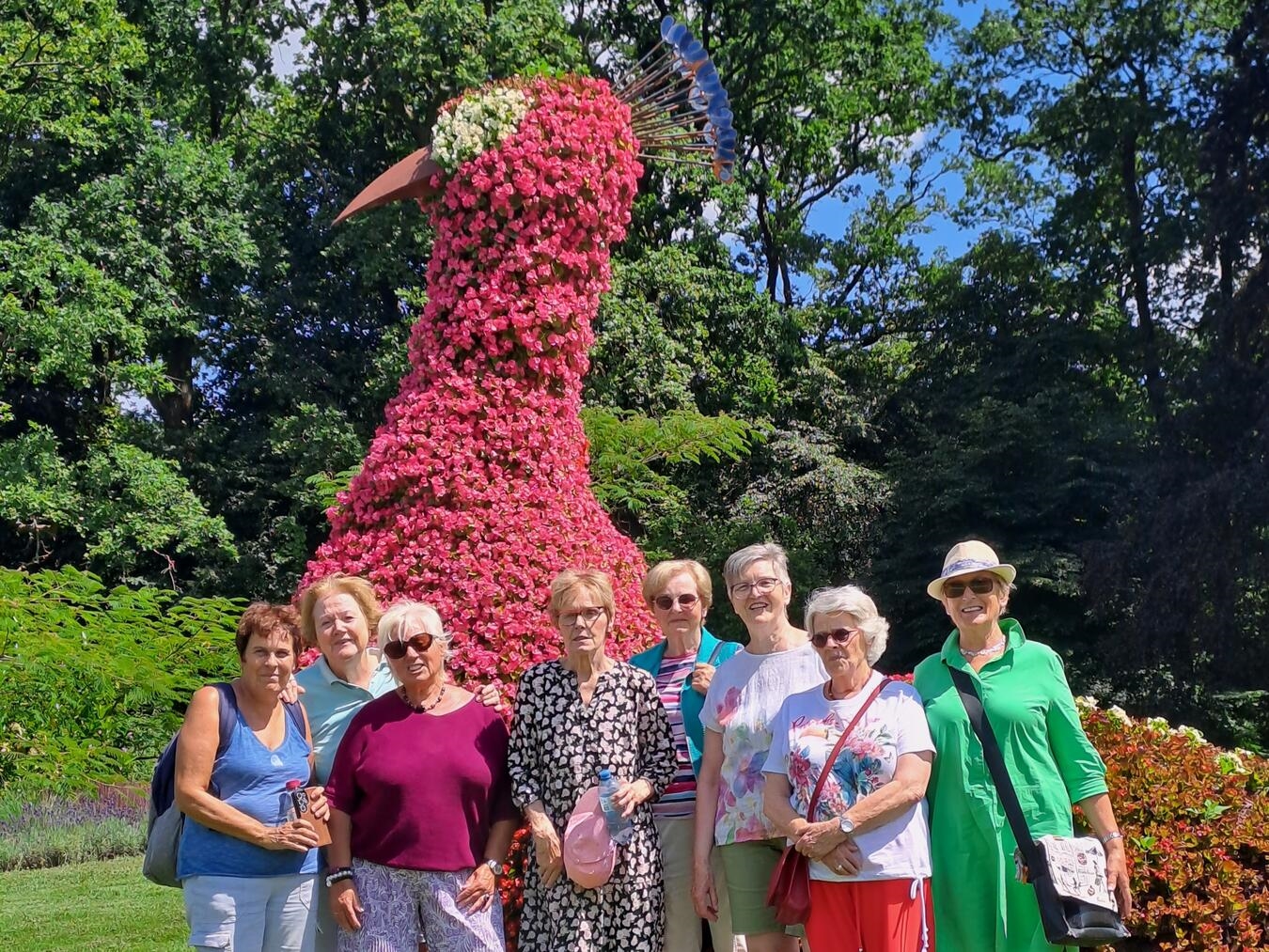 "Gruppenfoto vor farbenprächtigem Blumenpfau im Park"