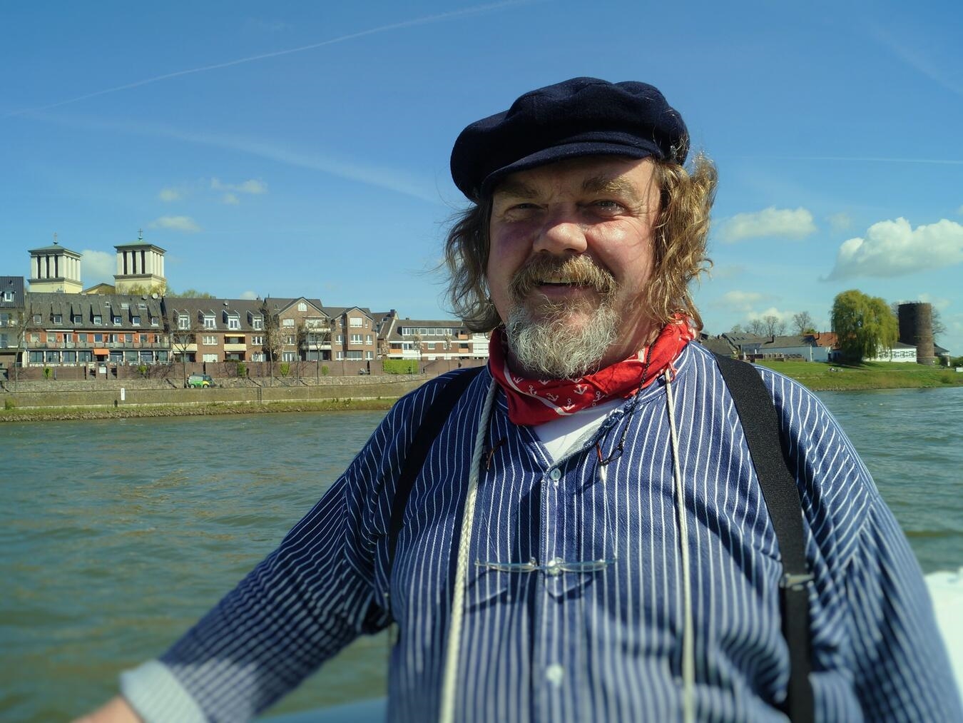 Heinz Wellmann als „Hein vom Rhein“ in traditioneller Tracht, lächelnd, vor einer malerischen Rheinlandschaft.