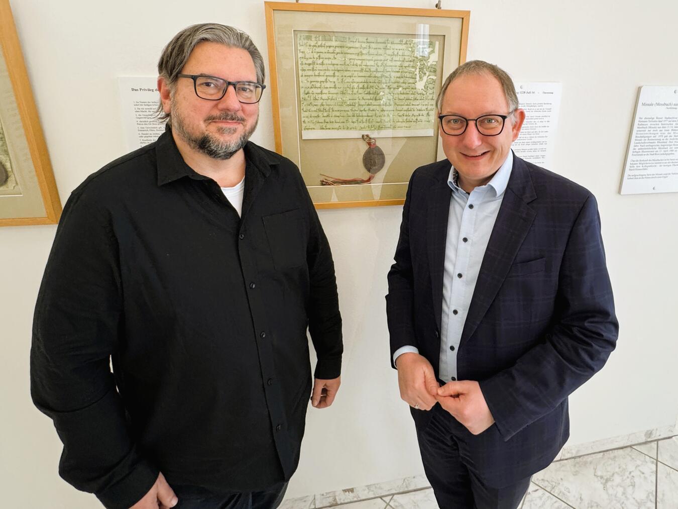Rees: Koordination für 800 Jahre In 2028 jährt sich die Reeser Stadterhebung zum 800. Mal. Michael Scholten (li., vor der historischen Urkunde mit Bürgermeister Sebastian Hense) hat im Rathaus die Projektkoordination für das große Jubiläum übernommen. Foto: Stadt Rees