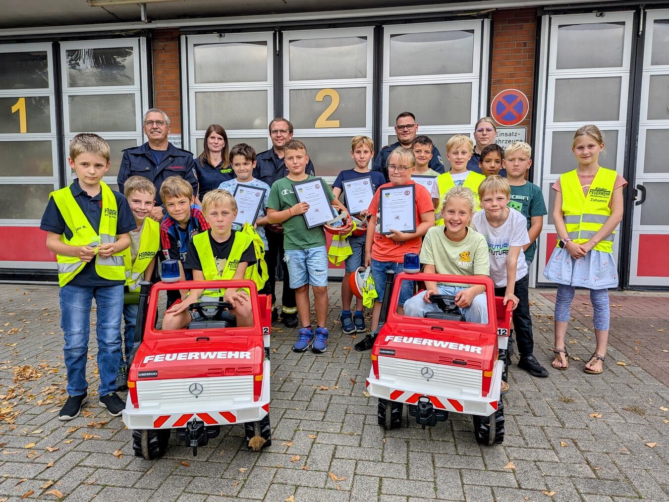 In der Mitte halten Moritz, Nico, Tarke, Julian und Noah stolz ihre Überstellungsurkunden in den Händen - sie wurden feierlich von der Kinder- in die Jugendfeuerwehr übernommen. Die anderen Kinder fieberten begeistert mit. Im Hintergrund gratulieren Feuerwehrleiter Klaus Elsmann (links) sowie die Leitungen der Kinder- und Jugendfeuerwehr zu diesem besonderen Schritt. Foto: Feuerwehr Bedburg-Hau