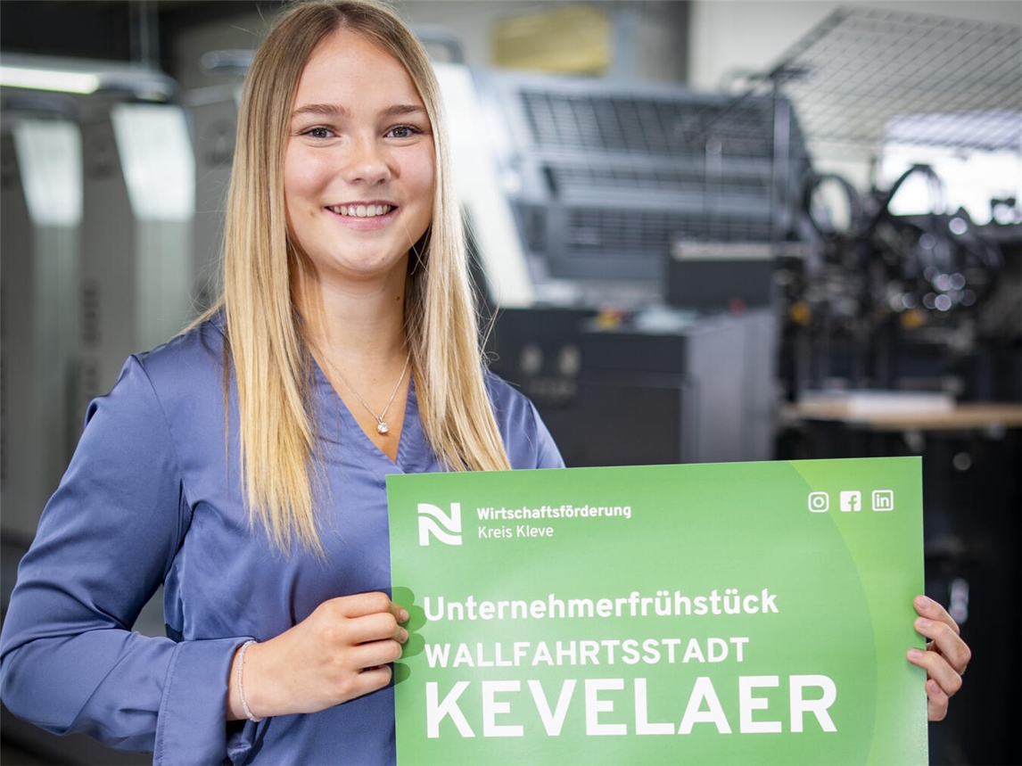 Ina Schulz, Auszubildende der Wirtschaftsförderung Kreis Kleve, präsentiert das Plakat mit der Einladung zum Unternehmerfrühstück in der Stadt Kevelaer. Foto: Gerhard Seybert