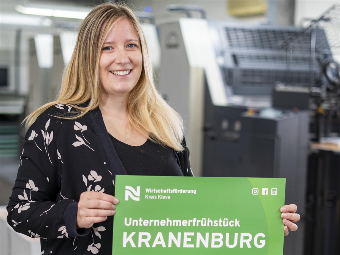 Irina Janßen von der Wirtschaftsförderung Kreis Kleve präsentiert das Plakat mit der Einladung zum Unternehmerfrühstück in Kranenburg. Foto: WfG/Gerhard Seybert