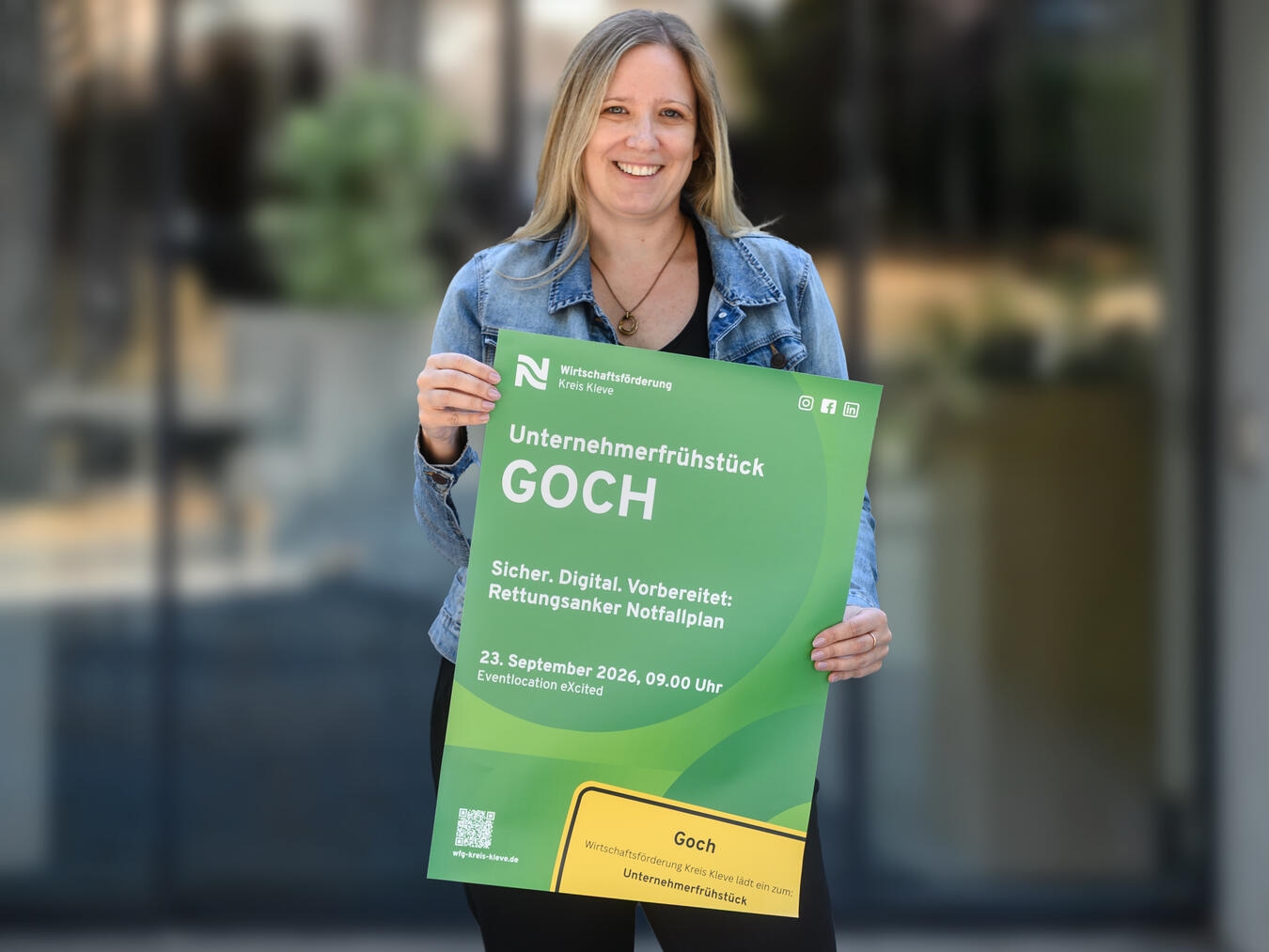 Irina Janßen präsentiert Plakat für Unternehmerfrühstück in Goch, organisiert von der Wirtschaftsförderung Kreis Kleve.