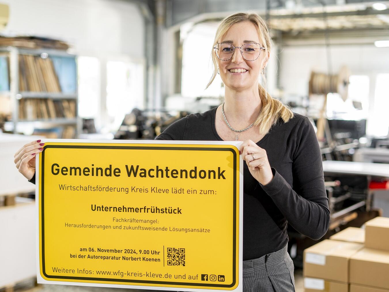 Irina Schultz von der Wirtschaftsförderung Kreis Kleve präsentiert das Ortsschild der Gemeinde Wachtendonk mit der Einladung zum Unternehmerfrühstück.Foto: WfG Kreis Kleve