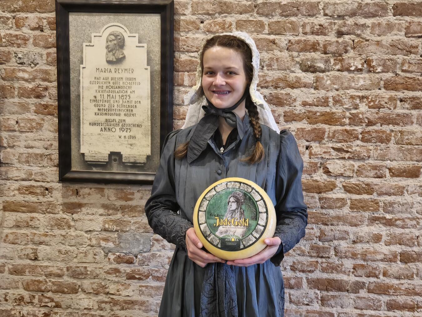 Isabelle Schulte Spechtel doubelt Maria Reymer und zeigt den zu Ehren der Pionierin entwickelten Käse „Jade Gold“, der am 11. Mai natürlich verkostet werden kann. NN-Foto: HF