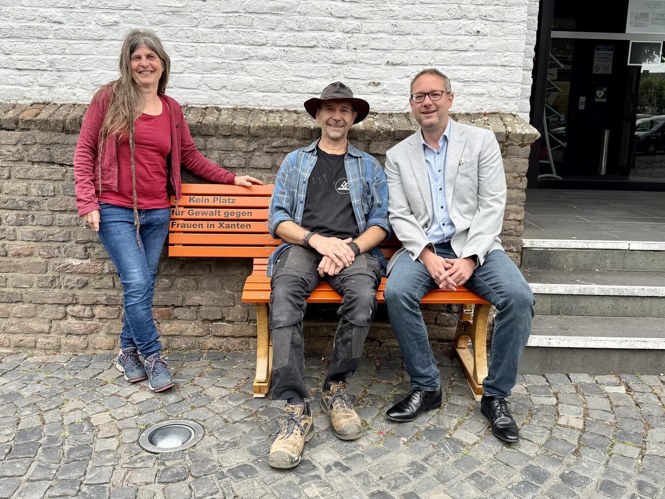 Jochen Cleve (APX), Stefan Haupt (Leiter APX-Holzwerkstatt) und Sabine Reuß (Gleichstellungsbeauftragte der Stadt Xanten; v.l.) mit der orangefarbenen Bank vor dem Xantener Rathaus. NN-Foto: SP