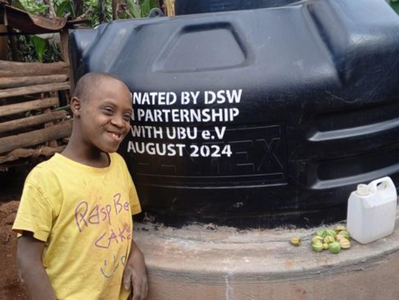 "Jonathan lächelt neben seinem grünen Regenwassertank im Garten, nachhaltige Wassernutzung"
